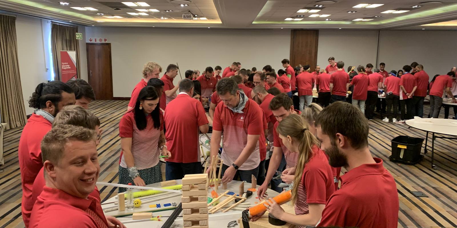 A conference room full of teams building one giant chain reaction machine