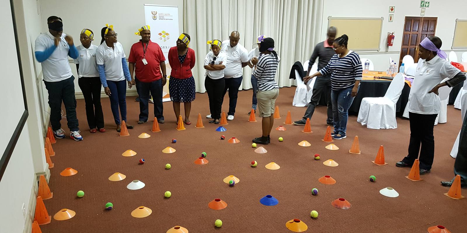 Colleagues guiding blindfolded team-mates through a field of cones by voice alone