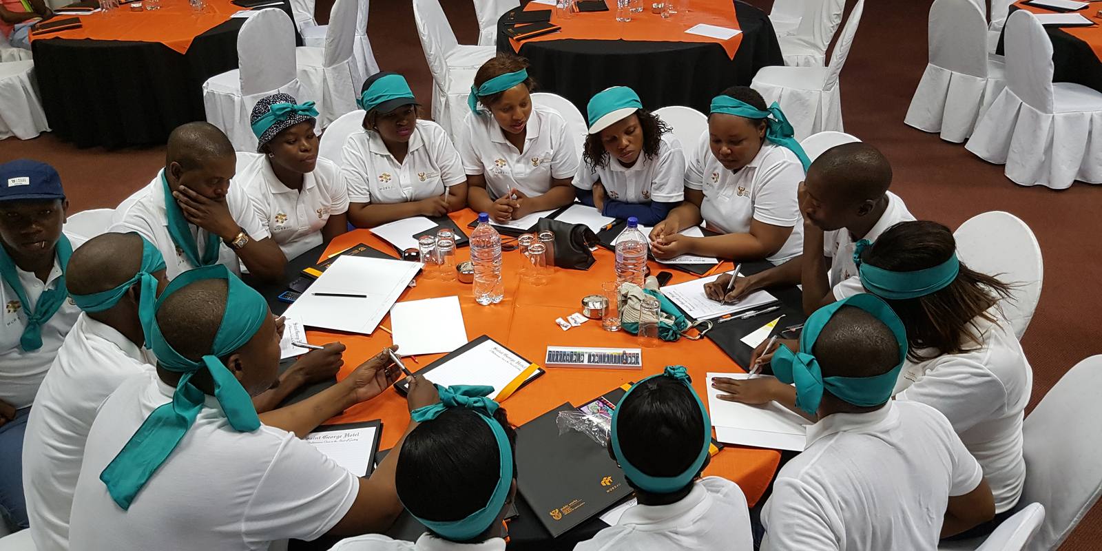 Teams in matching headbands planning around round tables during a facilitated programme