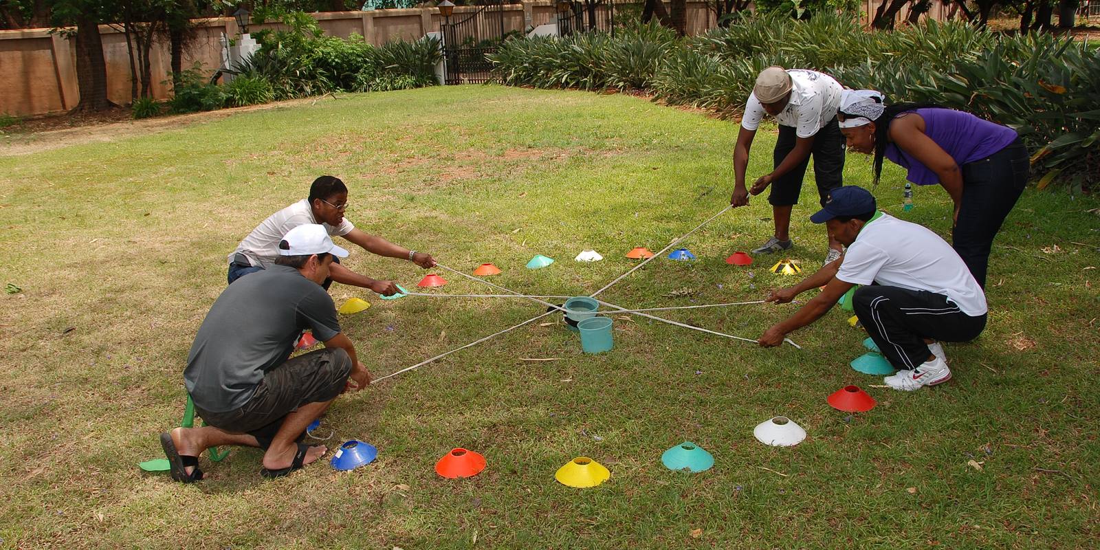 A team crouched around a rope-and-cone challenge, working out a plan together